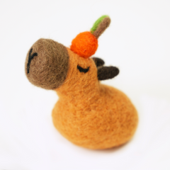 Small felted animal capybara with a carrot on a white background